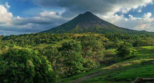 Central America - Costa Rica, lush greenery surrounding the majestic Arenal Volcano under a bright blue sky. 