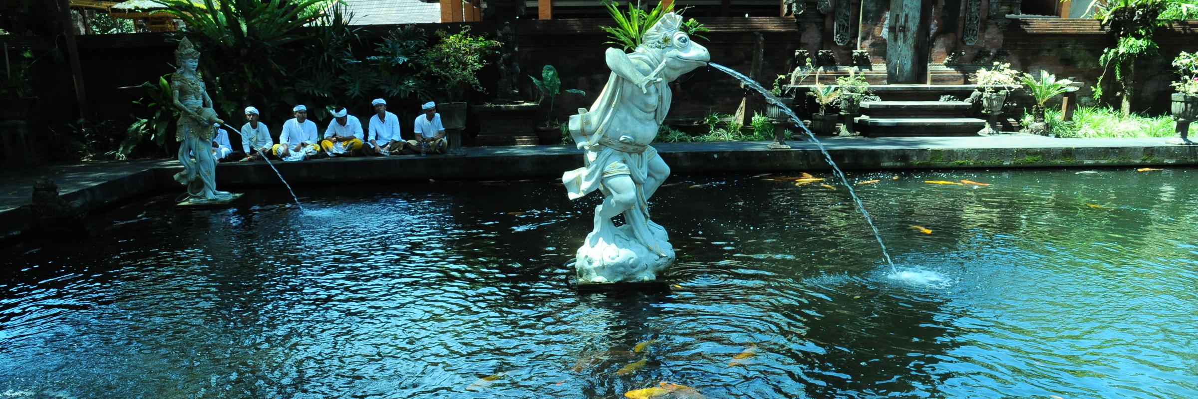 Colorful koi fish swim beneath stone fountains in a peaceful temple pond setting in Bali, Indonesia. 